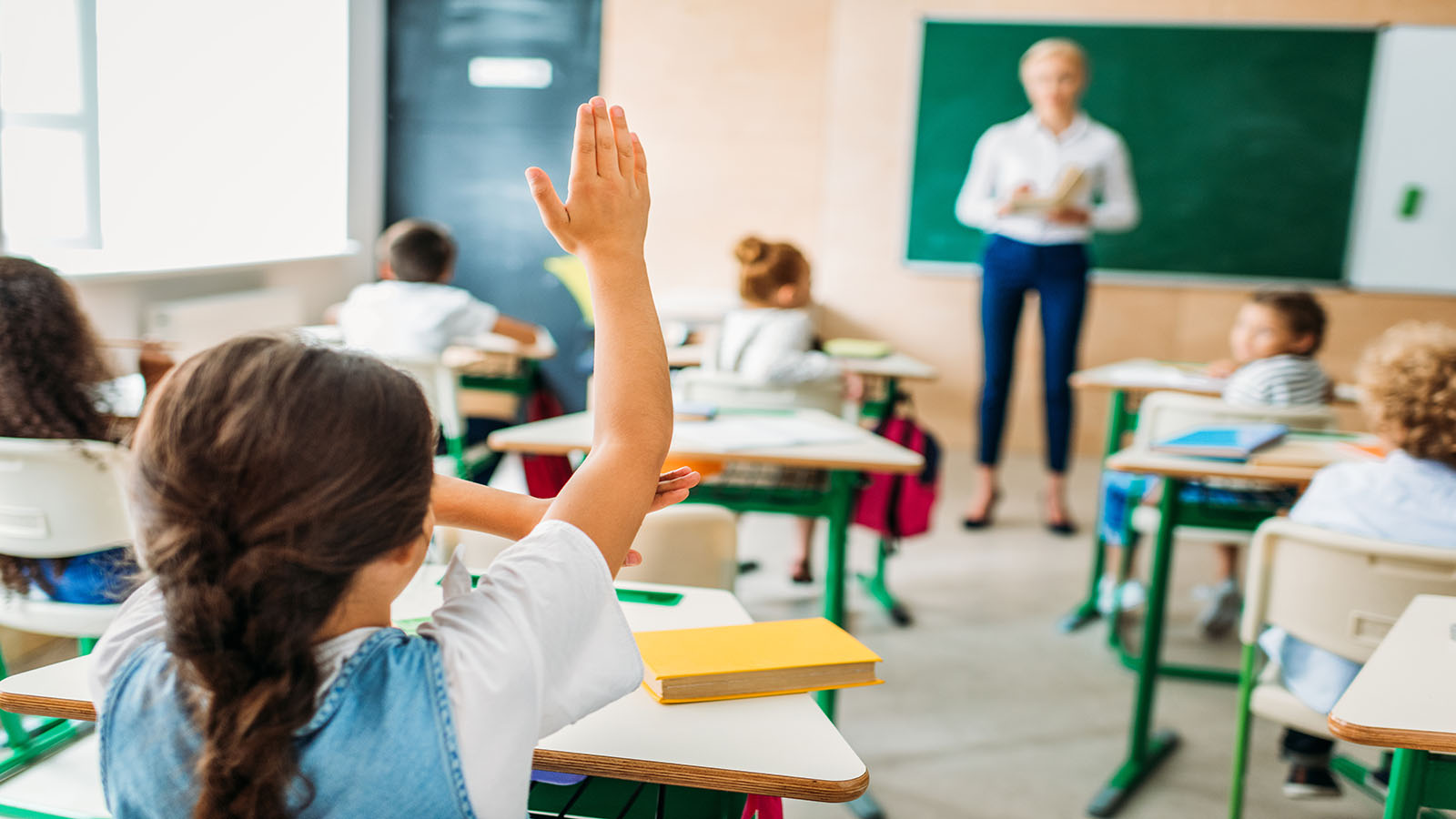 image of a rear view of schoolgirl raising hand to answer teachers question
